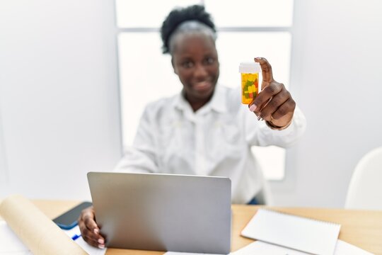 Young african american woman architect using laptop holding pills at architecture studio