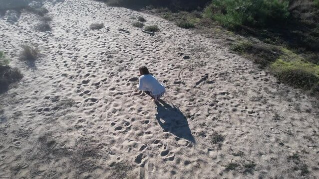 A brunette with a white shawl dancing estatic on sand