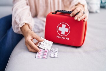 Middle age grey-haired woman holding pills and first aid kit at street