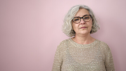 Middle age woman with grey hair standing with serious expression over isolated pink background