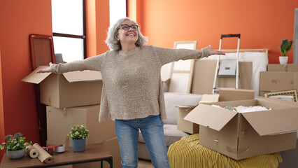 Middle age woman with grey hair smiling confident standing with arms open at new home - obrazy, fototapety, plakaty