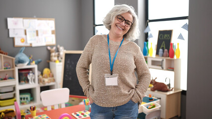 Middle age woman with grey hair preschool teacher smiling confident standing at kindergarten