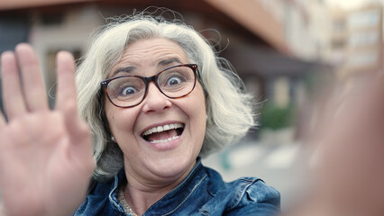 Middle age woman with grey hair smiling confident having video call at street