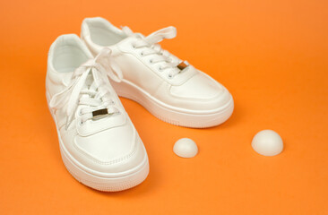 Sport shoes. Stylish white sneakers with untied laces. White sneakers on an orange background.