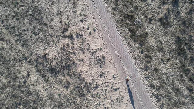 A yoga teacher walks on the wooden path between the beach and the forest, drone view taken from above