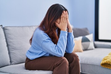 Fototapeta premium Young hispanic woman stressed sitting on sofa at home