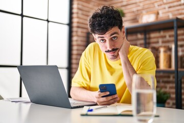 Young caucasian man using laptop and smartphone at home