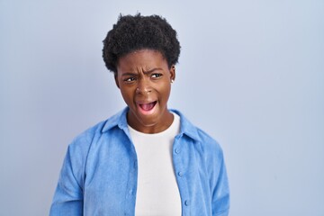 African american woman standing over blue background angry and mad screaming frustrated and furious, shouting with anger. rage and aggressive concept.