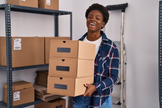 African american woman working at small business ecommerce holding boxes smiling and laughing hard out loud because funny crazy joke.