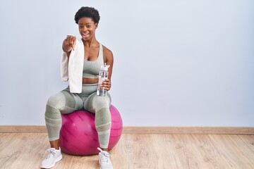 African american woman wearing sportswear sitting on pilates ball pointing to you and the camera with fingers, smiling positive and cheerful