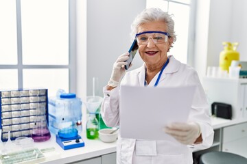 Senior grey-haired woman wearing scientist uniform talking on the smartphone at laboratory