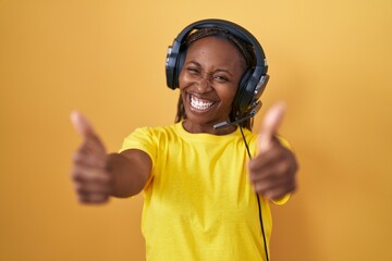 African american woman listening to music using headphones approving doing positive gesture with hand, thumbs up smiling and happy for success. winner gesture.