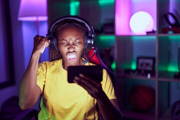 African american woman playing video games with smartphone annoyed and frustrated shouting with anger, yelling crazy with anger and hand raised