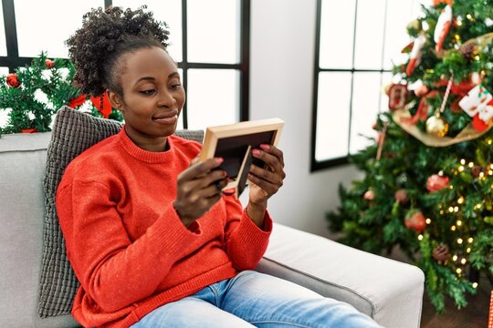 African american woman looking picture sitting on sofa by christmas tree at home