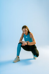 Woman sitting and looking at smartwatch checking her performance on studio background