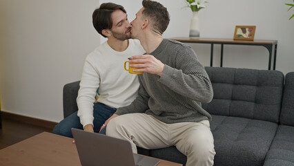 Two men couple using laptop drinking coffee kissing at home