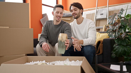 Two men couple unpacking cardboard box at new home