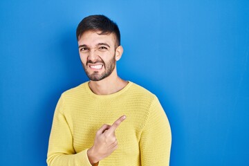 Hispanic man standing over blue background pointing aside worried and nervous with forefinger,...