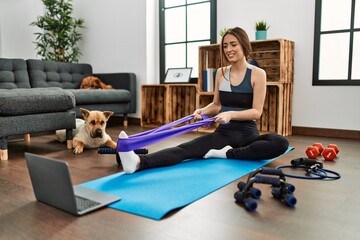 Young hispanic woman smiling confident having online traininig using elastic band at home
