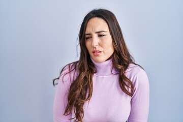 Obraz premium Young brunette woman standing over blue background with hand on stomach because indigestion, painful illness feeling unwell. ache concept.