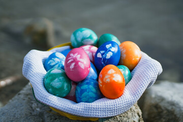 handmade colorful painted diy eco easter eggs in a basket or nest infront of a stony bavarian lake with blue water 
