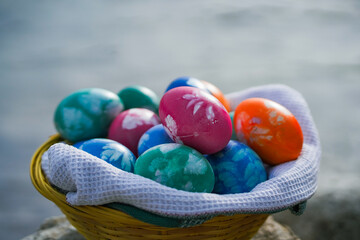 handmade colorful painted diy eco easter eggs in a basket or nest infront of a stony bavarian lake with blue water 
