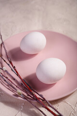 Easter table setting with pink plate, willow branches and two white eggs on white table.