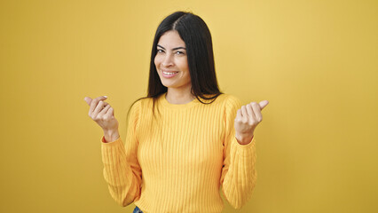 Young beautiful hispanic woman smiling confident doing money gesture over isolated yellow background