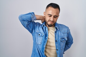 Young hispanic man standing over isolated background suffering of neck ache injury, touching neck with hand, muscular pain