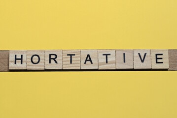 the word hortative of gray small wooden letters lies on a yellow table
