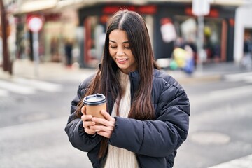 Fototapeta premium Young beautiful hispanic woman smiling confident drinking coffee at street