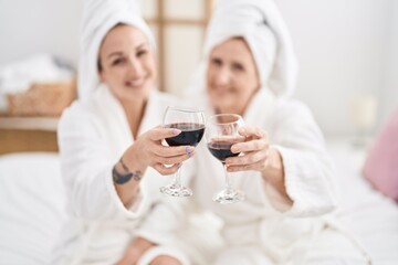 Obraz premium Mother and daughter wearing bathrobe drinking glass of wine at bedroom
