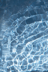 Abstract nature textured background, water waves in the pool with sun reflection. Clear water with bubbles and circles on blue background