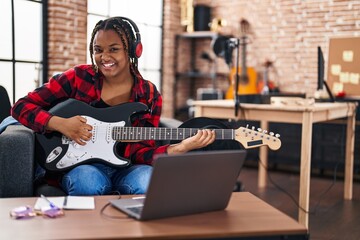 Fototapeta na wymiar African american woman musician having online electrical guitar lesson at music studio