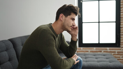 Young hispanic man sitting on sofa with serious expression at home