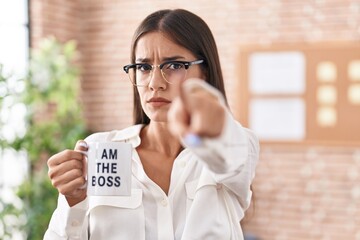 Young brunette woman drinking from i am the boss coffee cup pointing with finger to the camera and...