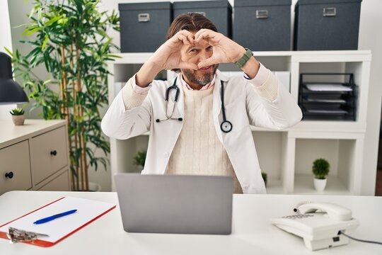 Handsome Middle Age Doctor Man Working At The Clinic Doing Heart Shape With Hand And Fingers Smiling Looking Through Sign