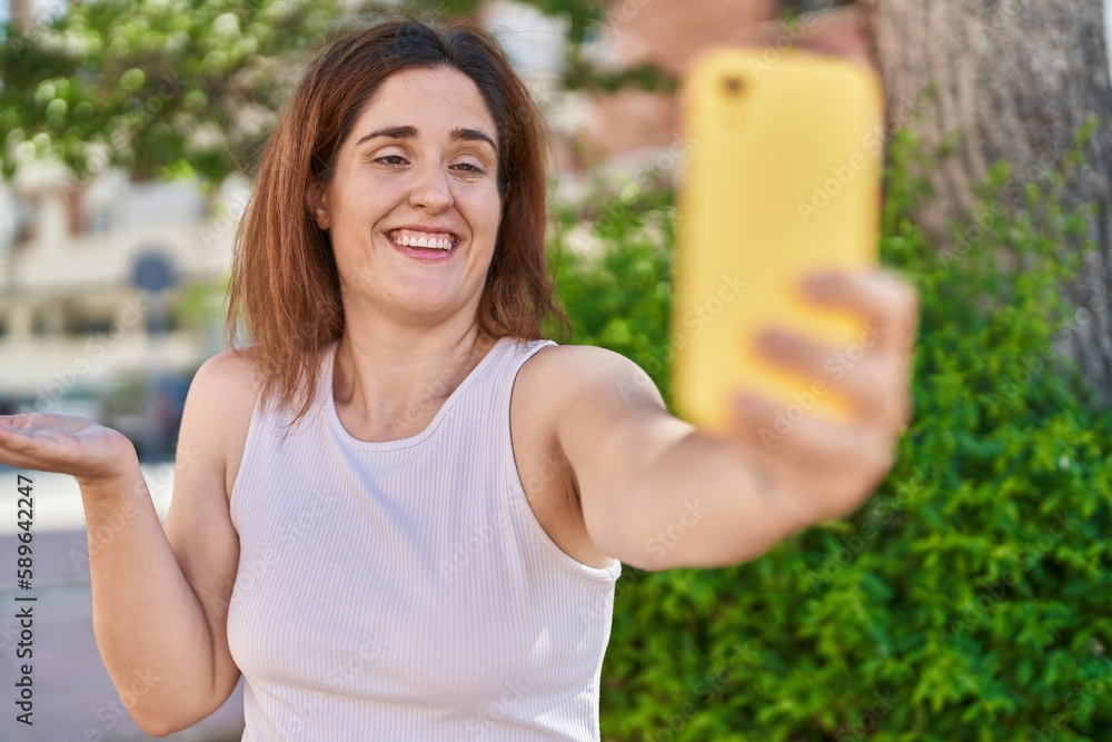 Wall mural Brunette woman taking a selfie photo with smartphone celebrating achievement with happy smile and winner expression with raised hand