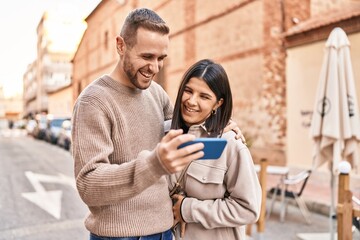 Man and woman couple smiling confident using smartphone at street