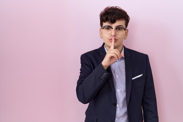 Young non binary man with beard wearing suit and tie asking to be quiet with finger on lips. silence and secret concept.