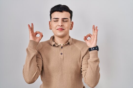 Non binary person standing over isolated background relaxed and smiling with eyes closed doing meditation gesture with fingers. yoga concept.