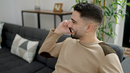 Young arab man talking on the smartphone sitting on sofa at home