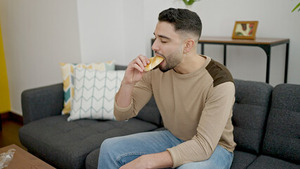 Young arab man eating cake sitting on sofa at home