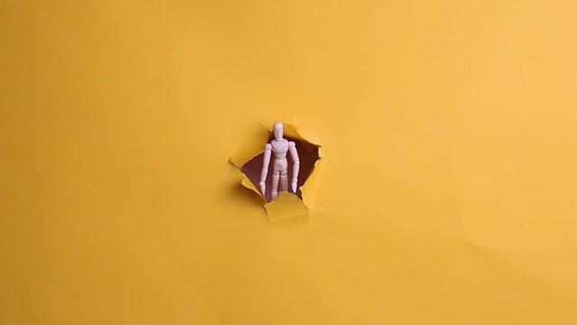 Wooden puppet peeking out of a hole on a yellow background.