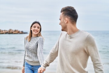 Man and woman couple smiling confident walking with hands together at seaside