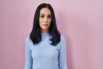 Fototapeta premium Hispanic woman standing over pink background relaxed with serious expression on face. simple and natural looking at the camera.