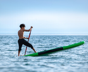 a sporty guy swims on a sup board with a paddle on the sea during the day against a beautiful sky