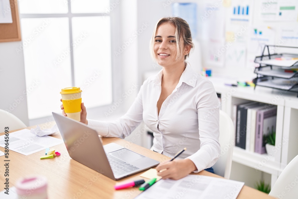 Poster young blonde woman business worker writing on reminder paper holding coffee at office