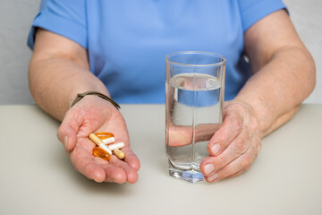 Senior woman with wrinkled old hands at the table holding various capsules, vitamins and pills for treatment. Healthcare and medicine concept