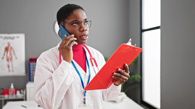 African american woman doctor talking on smartphone reading document at clinic